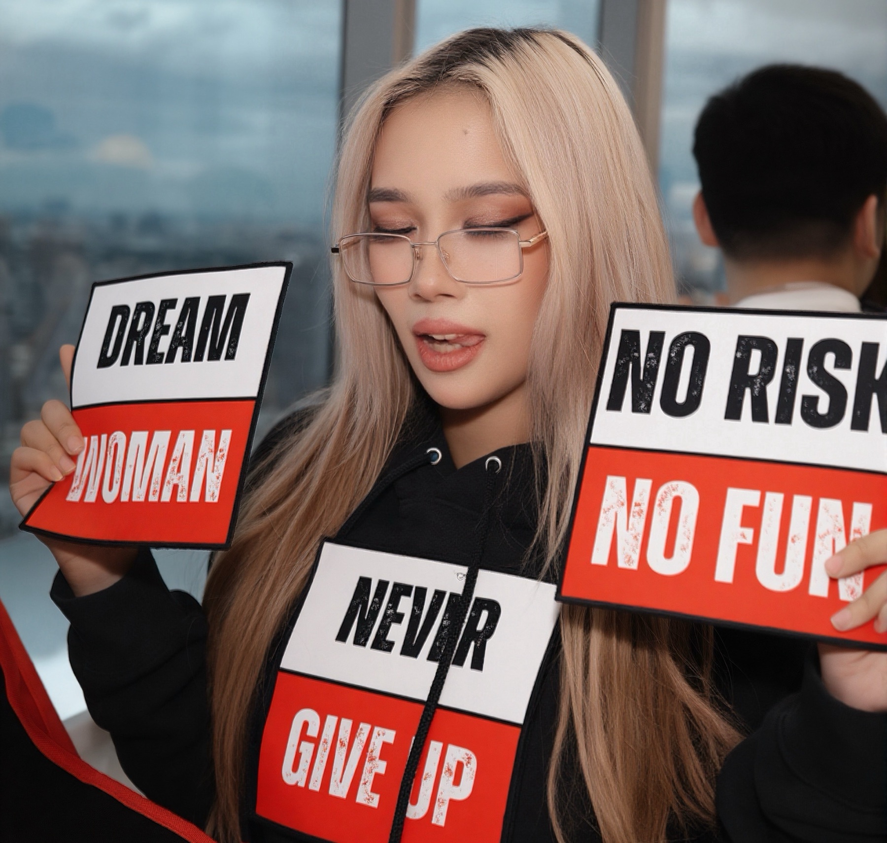 The model wearing the Never Give Up hoodie while holding up the Dream Woman and No Risk No Fun patches, showing the interchangeable system up close